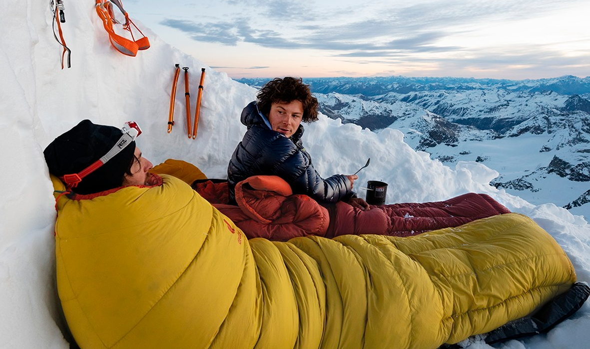 Saco de dormir rojo tumbado en la nieve en las montañas ropa cálida de  invierno y equipo para actividades al aire libre